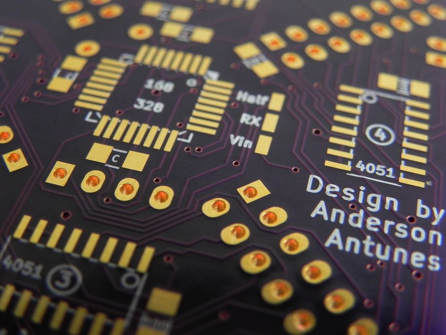 Close-up artístico da placa de circuito impresso com acabamento dourado e componentes soldados.