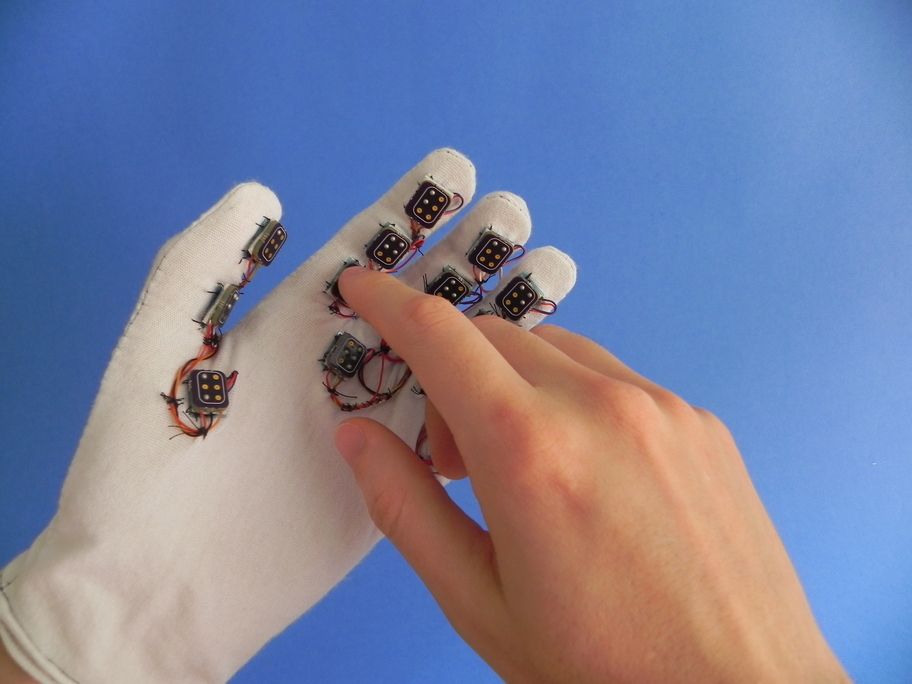 Dedo da mão direita tocando um dos pontos interativos na palma da mão esquerda vestindo a luva.